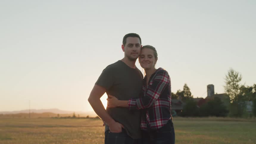 A couple embraces in a sunlit open field during golden hour