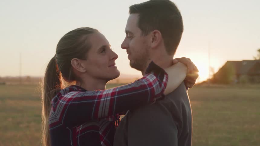 Young couple hug each other romantically while standing outdoors at sunset