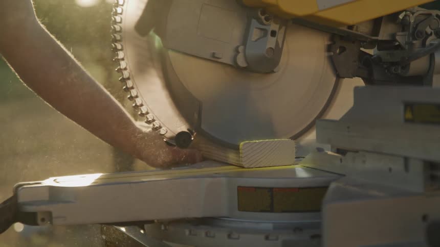 A person is operating a circular saw to cut a piece of wood in golden sunlight