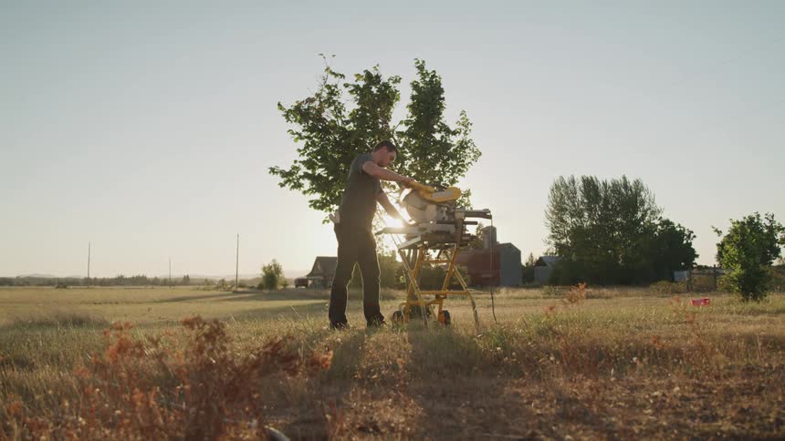 A man operates a table saw in a large open field under a clear sky