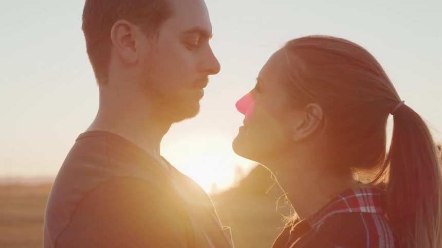 A man gently kisses a womans forehead as they embrace outdoors at sunset
