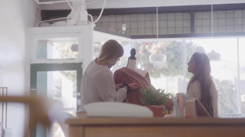 Two women are working together to drape fabric over a mannequin in a well lit fashion studio