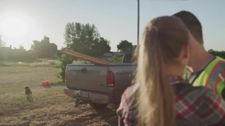 Man in work vest kissing his wife goodbye while both are in a field