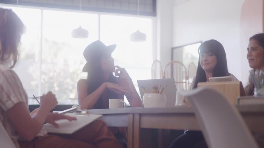 Women discussing work around a table in a bright room