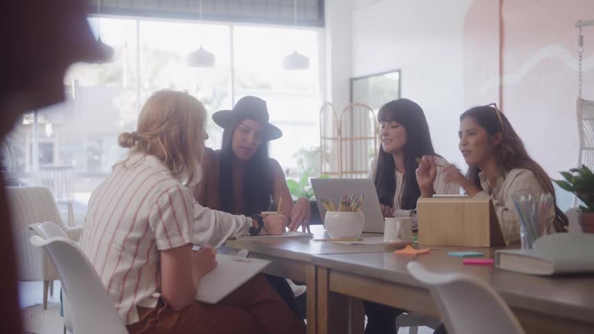 Group of women at a table with objects talking