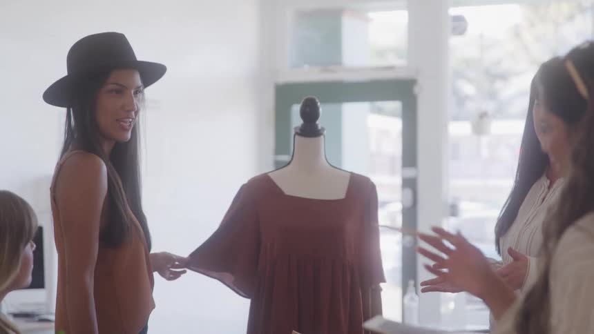 A group of fashion designers are gathered around a mannequin discussing a design in a bright studio