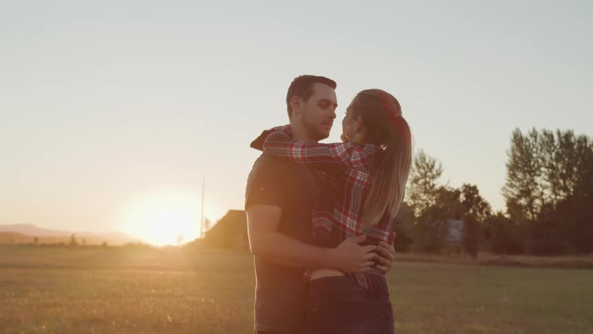 A couple embraces while gazing into each others eyes during sunset in an open field