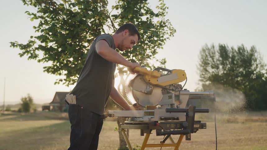 A man operates a circular saw to cut wood outdoors on a sunny day