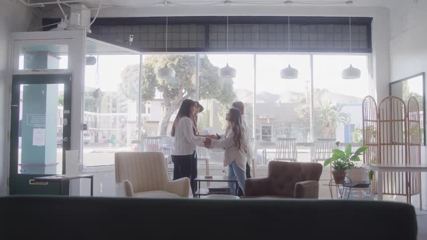 Friends are happily greeting each other inside a brightly lit modern cafe or lounge