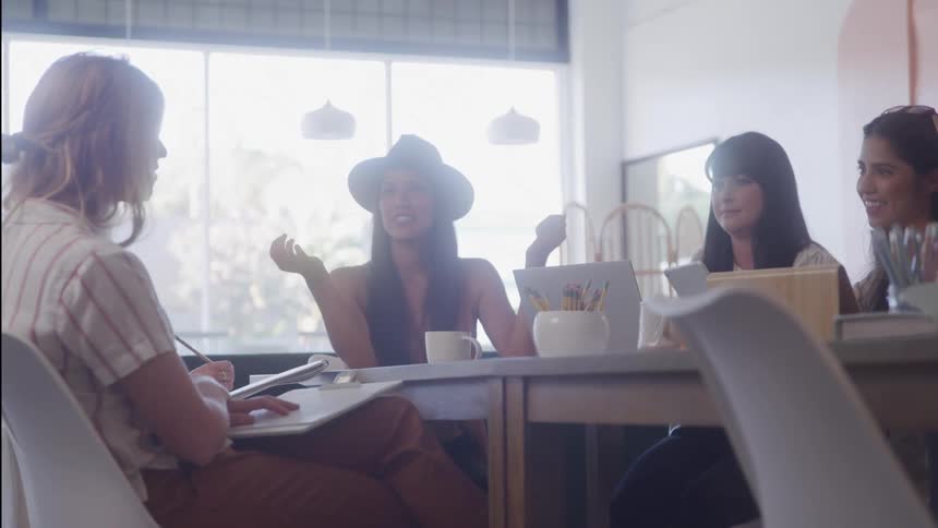 4 women talking at a table with one of them taking notes on paper
