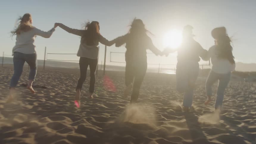 Women are running and holding hands on the beach