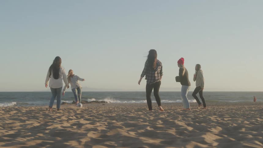 A group of young women walk and hang out together on a sandy beach near the ocean