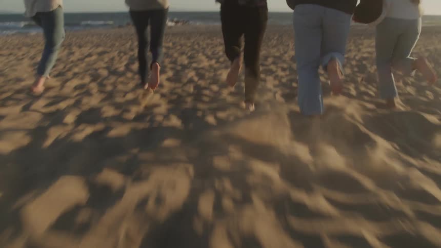 A group of friends is running barefoot on the sandy beach toward the ocean