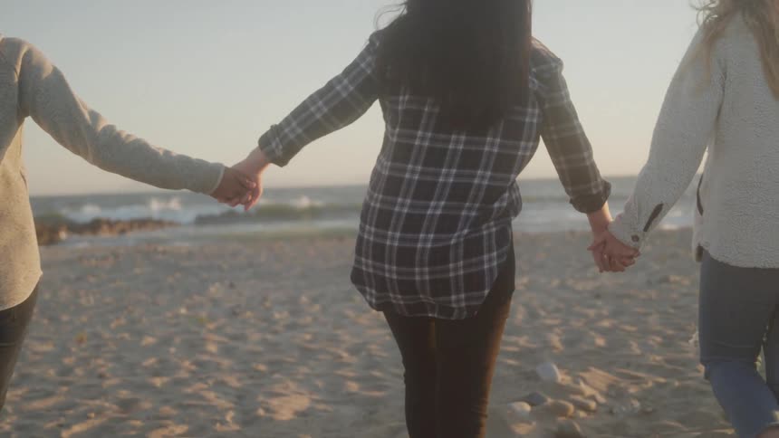 Women holding hands walking on the sand at the beach