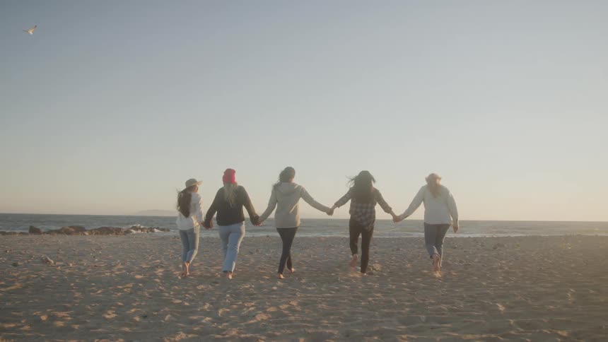 Five people walk hand in hand on a beach at sunset