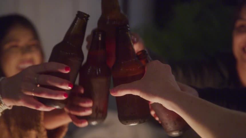 Friends cheerfully clink beer bottles together in a celebratory toast