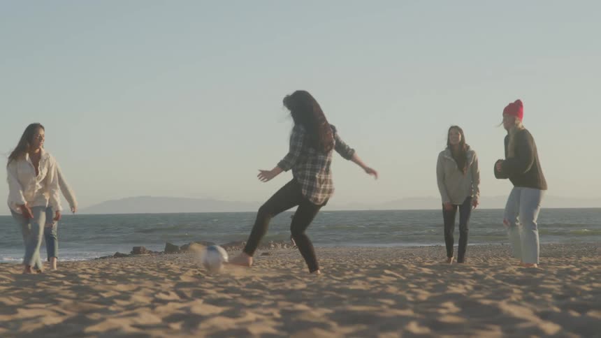 Five women passes football around on the beach sand in the evening