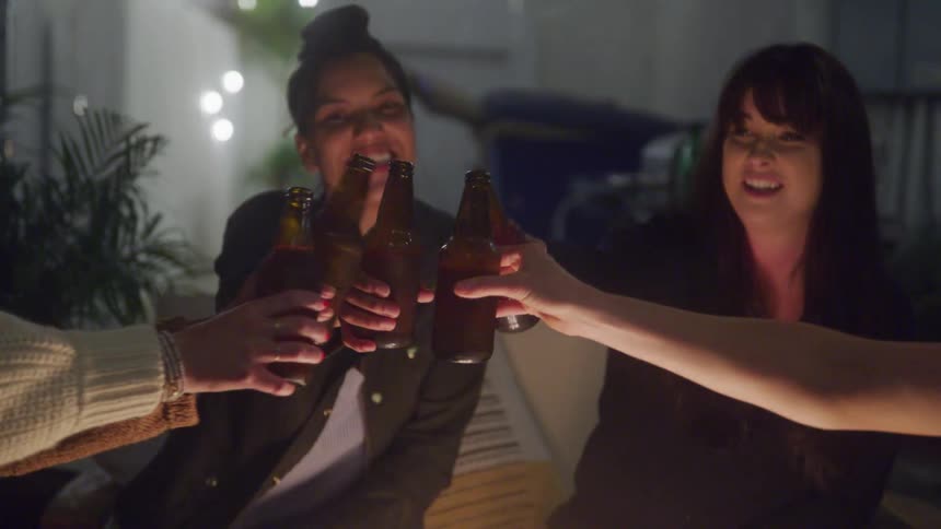 Friends toast with beer bottles around a cozy outdoor setting at night