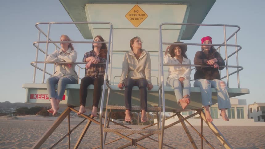 Five people sit barefoot on a lifeguard tower enjoying the beach scenery together