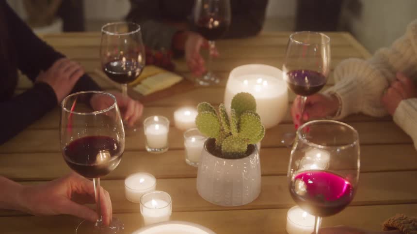 Friends enjoy a cozy evening with wine and candles around a wooden table