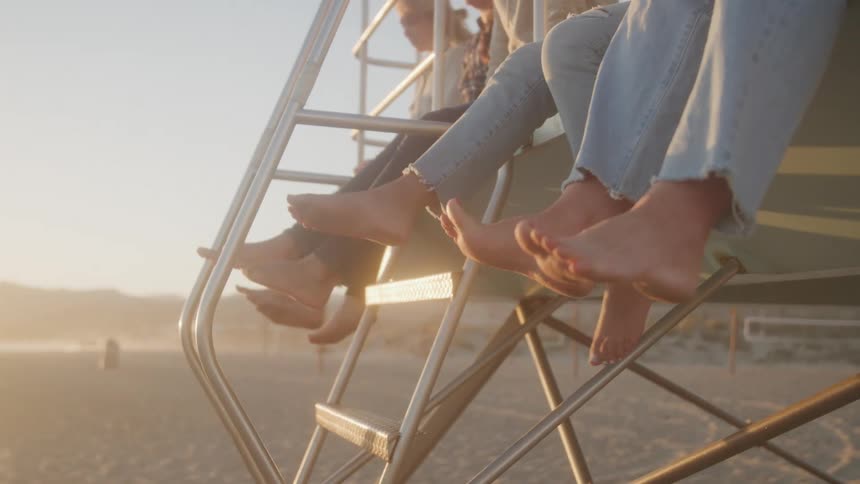 4 women on a high platform at the beach swinging their bare feet