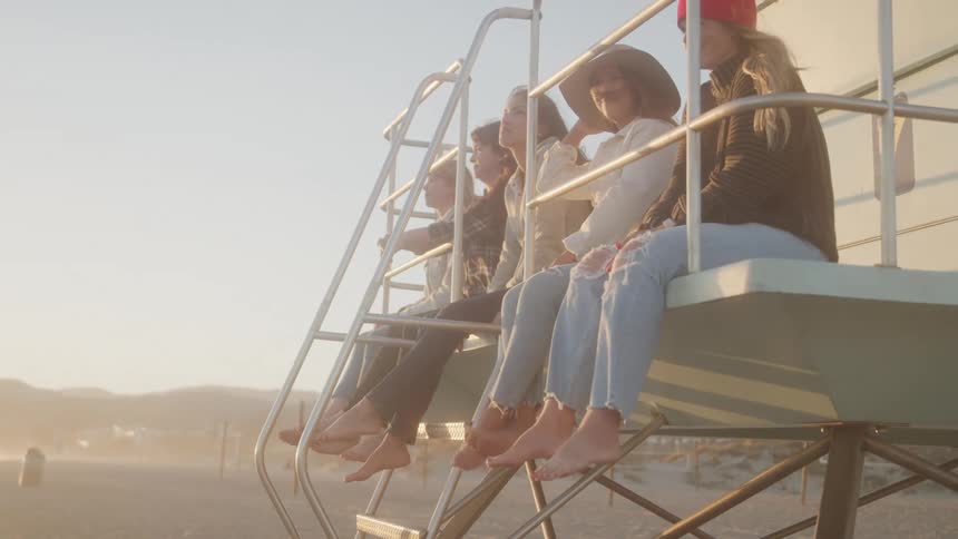 Five women sit on a coast guard house two of them wearing hats on a sunny day