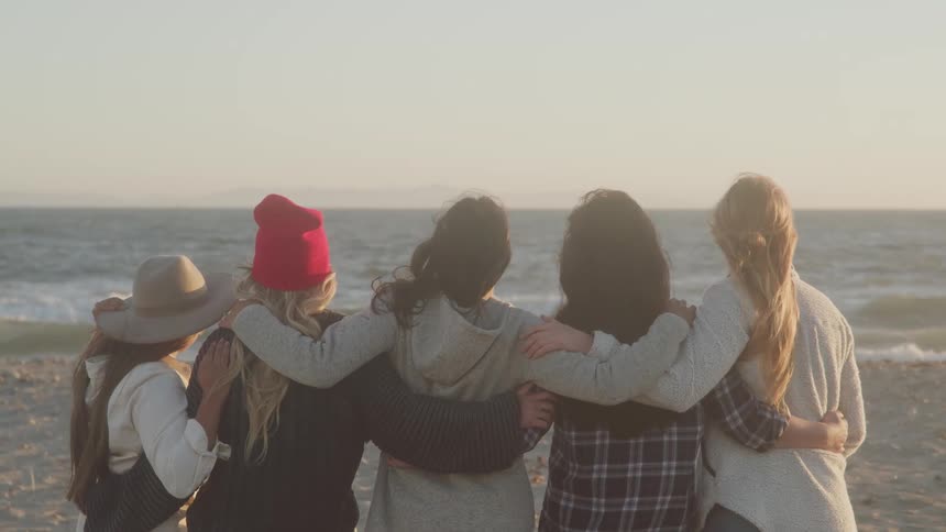 Women stand on the beach with their arms around each others shoulders
