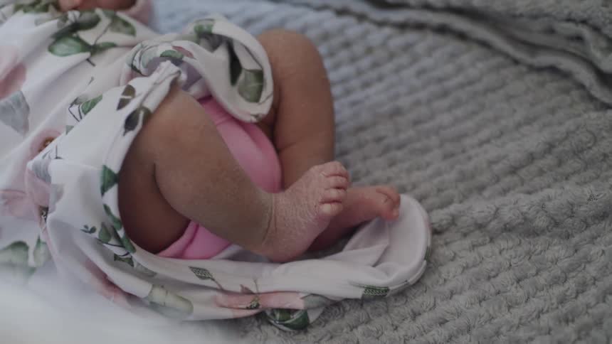 A newborn babys feet peek out from a floral blanket on a soft textured surface