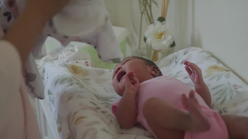 A baby in a pink onesie lies on a changing pad while an adult tends to them