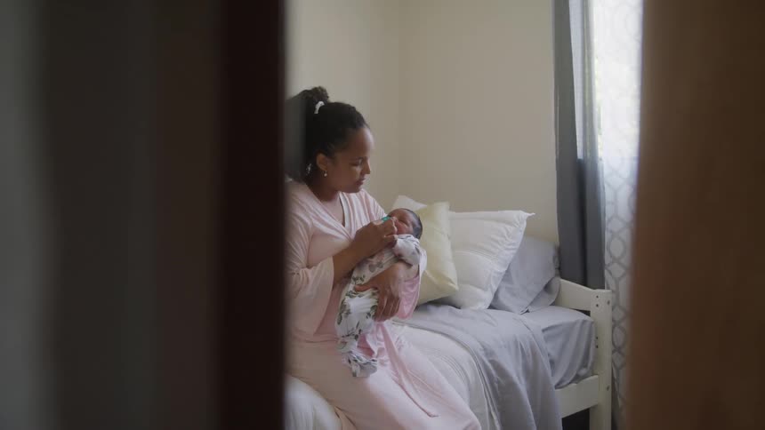 Mother with sleeping baby daughter on her lap sitting on a bed