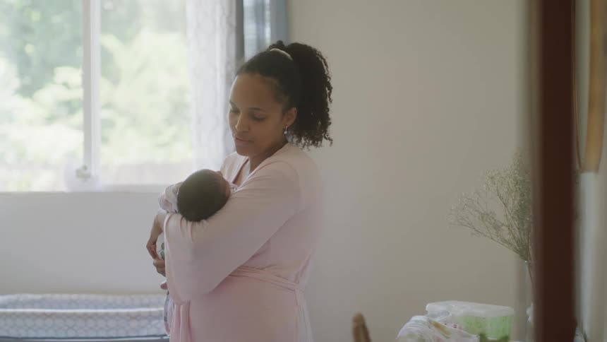 A woman is holding her baby by the window