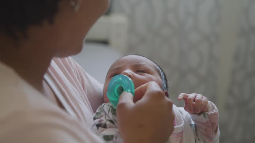 Mother giving pacifier to newborn daughter