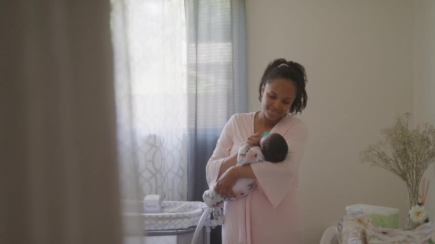 A mother gently cradles her baby while standing in a softly lit nursery
