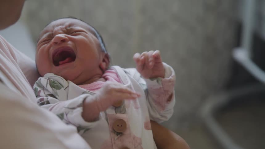 Close up of a baby crying in his mothers arms in a room during daytime