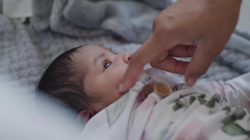 A baby looks up while gently sucking on an adults finger