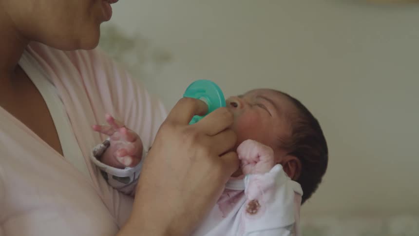 A woman gently feeds a newborn baby with a pacifier while cradling it in her arms
