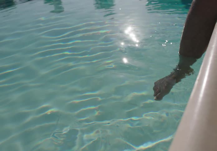 Leg submerged up to the knee in a swimming pool reflects sunlight on the surface of the clear water