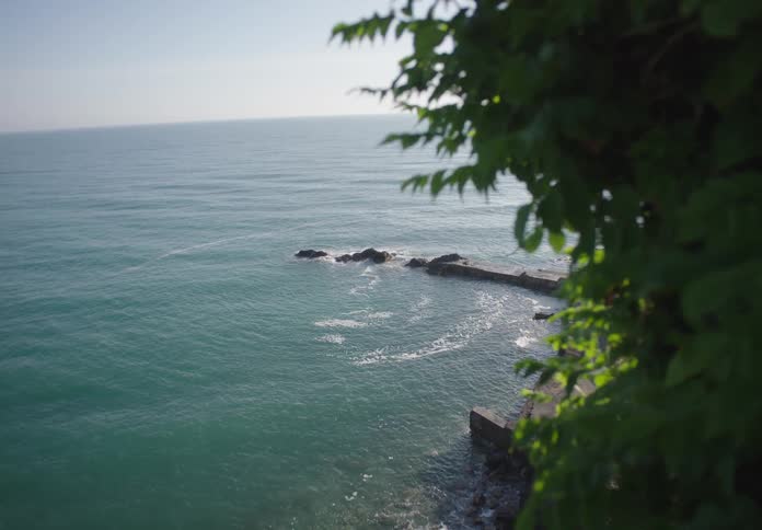 Calm ocean waves meet a stone pier framed by greenery