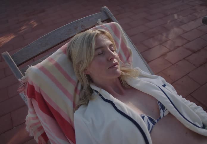 A woman wearing a swimsuit lies on a pool lounge chair around midday