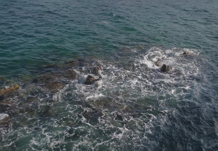 Waves crash against rocks on the shore in the ocean around midday