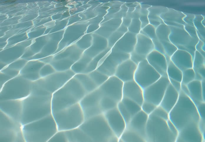Sunlight creates intricate wavy patterns on the surface of clear shallow water