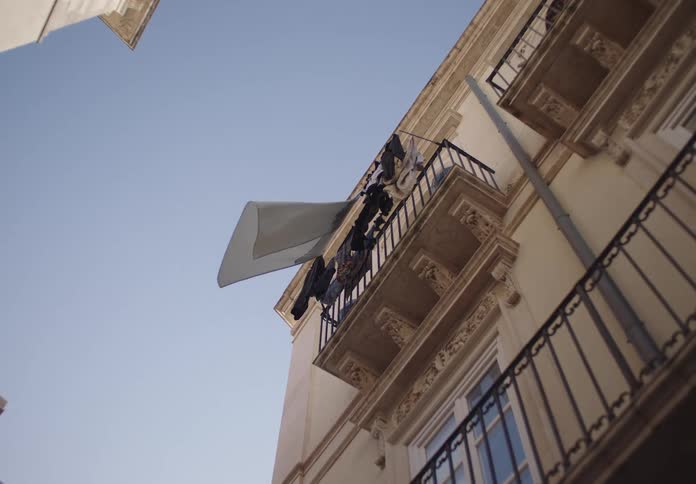 A low angle view shows laundry hanging on a balcony of a building with ornate details under a bright sky