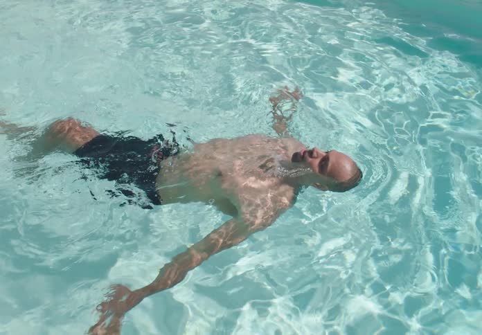 The man is swimming on his back in the pool