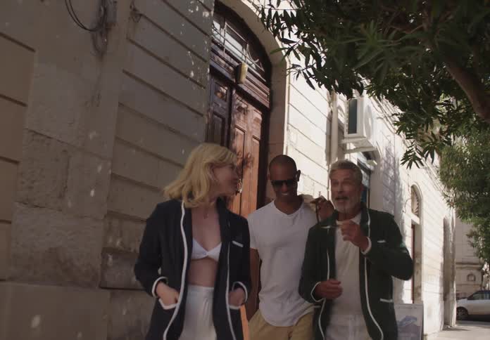 Two men and a woman walking down a city sidewalk talking happily