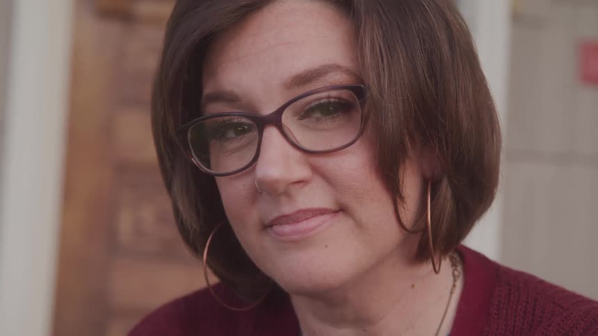 A woman smiles softly at the camera in a relaxed setting