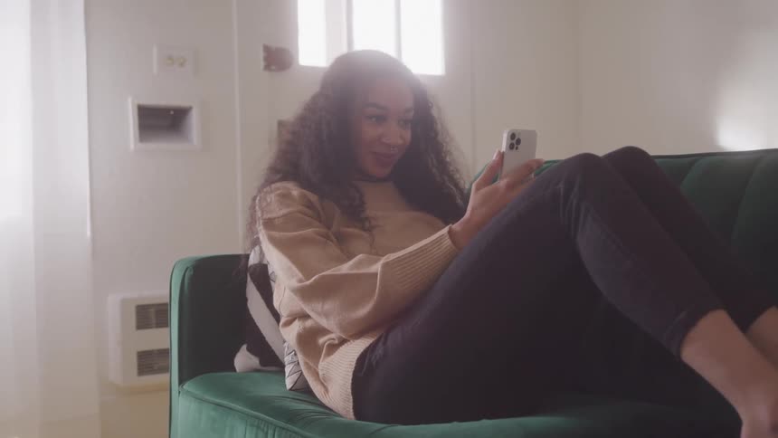 Young woman relaxes on a couch while smiling during a video call