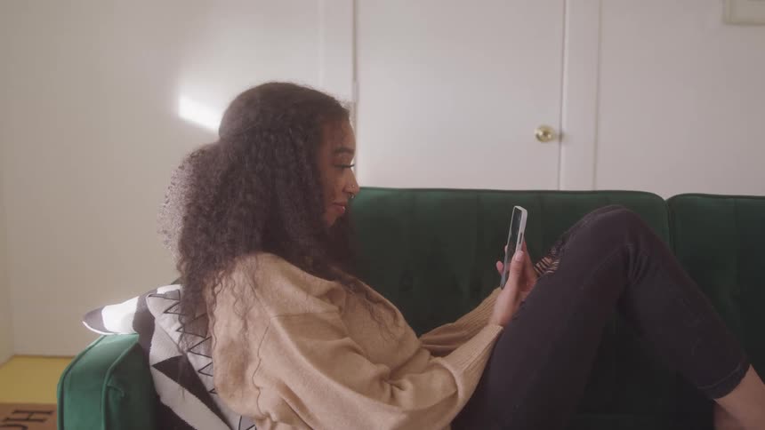 A woman sitting on the couch nods at her cell phone