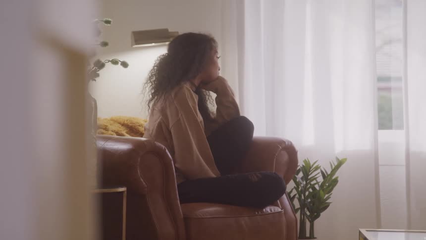 A woman sits on an arm chair and looks out the window