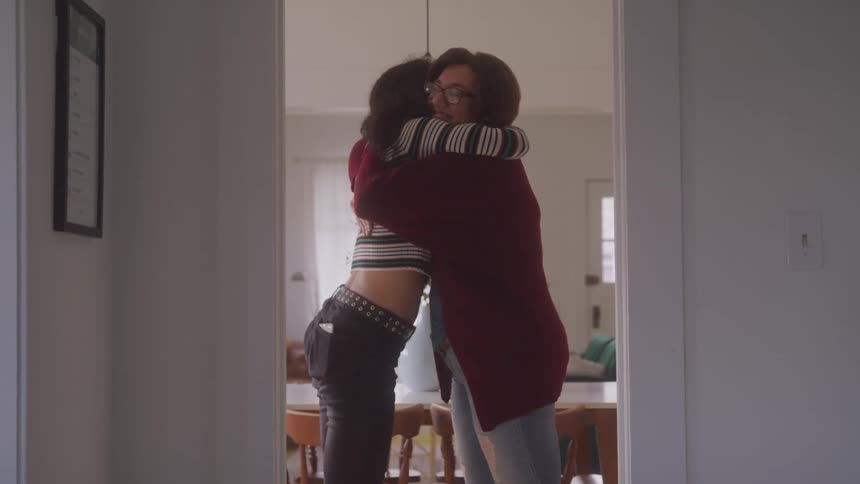 Mother and daughter share a warm hug in a doorway smiling in a cozy indoor setting