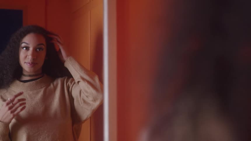 A girl smiles while adjusting her hair in the mirror